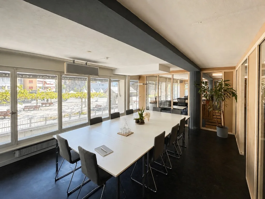 Salle de conférence à louer à Sion — grande table, fenêtres Place du Midi, jusqu'à 14 personnes